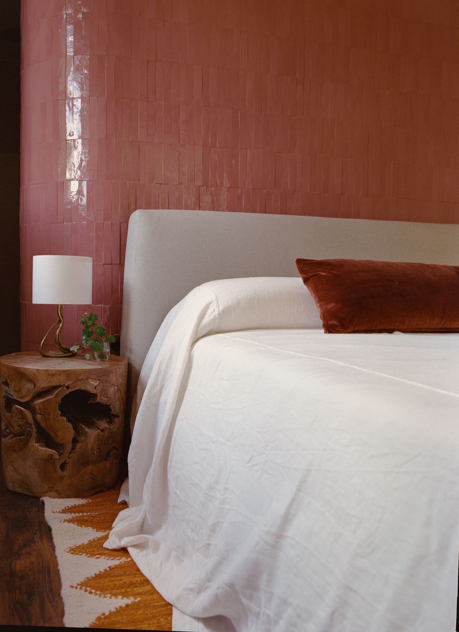 Bedroom with terracotta wall, white linen and a timber stool