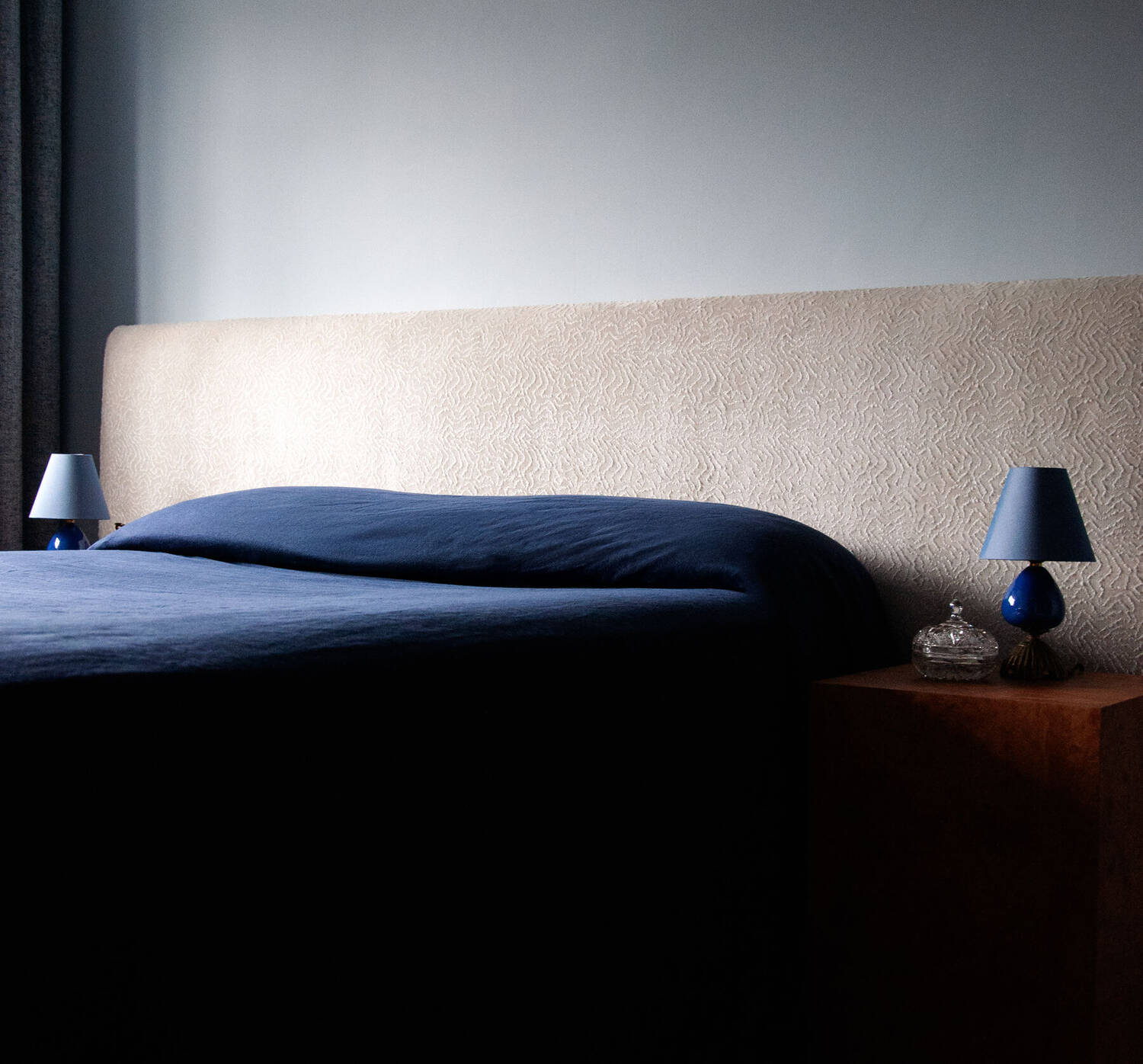 Bed dressed in deep navy with soft side lighting